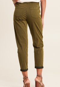 Pantalons vert olive fuselés avec une taille élastique et deux poches arrière. Ourlets roulés au niveau des chevilles, fabriqués dans un tissu léger.