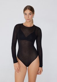 Schwarzer, transparenter, langärmeliger Bodysuit mit rundem Ausschnitt und figurnahem Design, der einen dezenten dreieckigen Akzent am Brustbereich aufweist. Sanfte Textur.