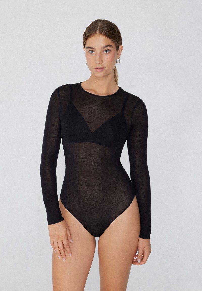 Schwarzer, transparenter, langärmeliger Bodysuit mit rundem Ausschnitt und figurnahem Design, der einen dezenten dreieckigen Akzent am Brustbereich aufweist. Sanfte Textur.