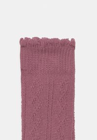 Strikkede sokker i myk rosa med et strukturert mønster og en volangkant øverst, med en jevn overflate og jevne sting.