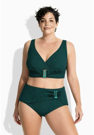 Frau mit kurzen lockigen Haaren, die einen zweiteiligen Badeanzug in Grün und Schwarz im Karomuster trägt, mit Schnallen am Oberteil und hoch taillierten Hosen.