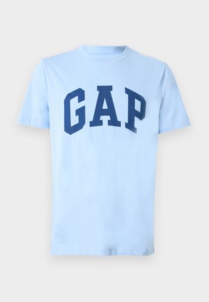 Világoskék pamut póló, amelyen vastag tengerészkék "GAP" logó látható a mellkas közepén. Rövid ujjú, klasszikus, kerek nyakkivágással.