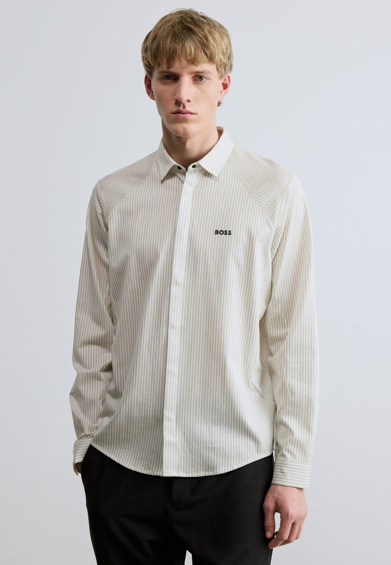 Ilgas rankovės marškiniai šviesiai kreminės spalvos su subtiliomis vertikaliomis juostelėmis ir juodu „BOSS“ logotipu kairėje krūtinės pusėje. Lygus audinys; prigludusi iškirptė.