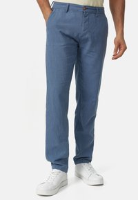 Hellblaue gestreifte Hose aus weichem Stoff, mit Knopfverschluss und Seitentaschen, kombiniert mit weißen Turnschuhen.