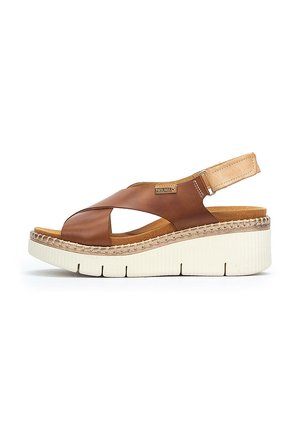 Sandalias de cuña de cuero marrón con un diseño de tira cruzada, media suela blanca gruesa y suela texturizada. Presenta una hebilla en la correa del talón.