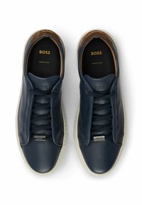 Tennarit tummansinisestä nahasta, joissa on sileä pinta. Kenkissä on nauhakiinnitys, kontrastoiva valkoinen kumipohja ja kohokuvioitu logo kielen päällä.