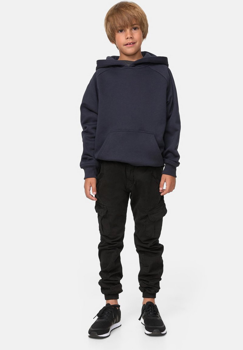 Felpa blu navy con tasca frontale e polsini a costine, abbinata a pantaloni cargo neri con tasche laterali e polsini elasticizzati. Sneakers nere.