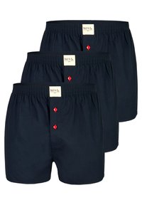 Trois paires de boxers en coton bleu marine avec une ceinture élastique et une braguette à boutons avec des boutons rouges. Des étiquettes sont visibles sur la ceinture.