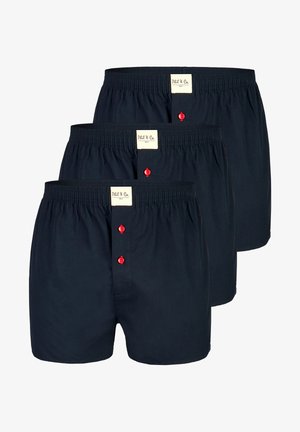 Drie paar marineblauwe katoenen boxershorts met een elastische tailleband en een knopenfly met rode knopen. Labels zijn zichtbaar op de tailleband.