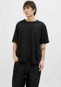 T-shirt noir surdimensionné en coton, avec un col rond et un petit détail de texte brodé en bleu sur la poitrine.