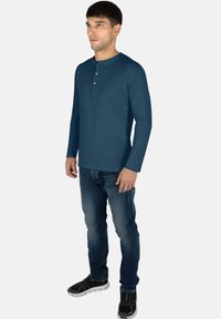 Langärmliges navy Henley-Shirt mit Rundhalsausschnitt und dreiknöpfiger Blende, kombiniert mit blauen Jeans und schwarzen Turnschuhen.