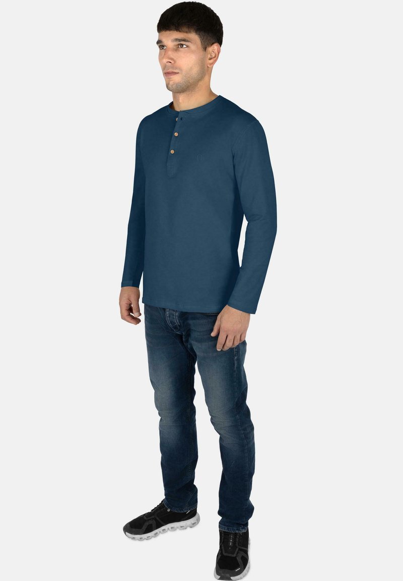 Langärmliges navy Henley-Shirt mit Rundhalsausschnitt und dreiknöpfiger Blende, kombiniert mit blauen Jeans und schwarzen Turnschuhen.