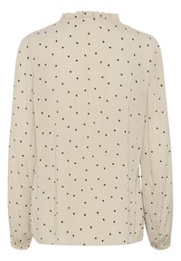 Blouse beige à manches longues avec des pois noirs, un col à volants et des poignets élastiqués. Tissu doux et léger avec une coupe décontractée.