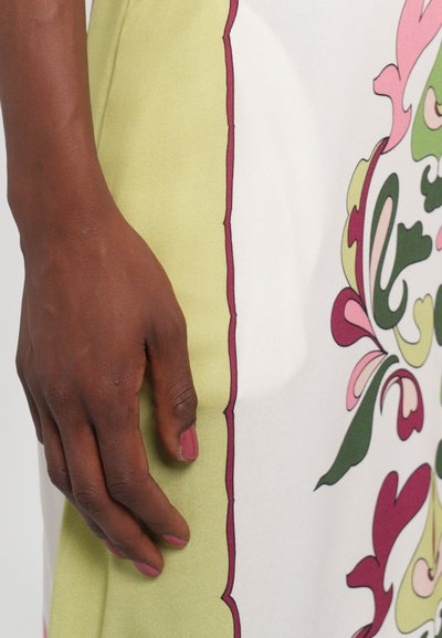 Floral-patterned dress with a white base, green accents, and maroon outlines. Fabric appears smooth with vibrant colors. Hand rests beside the dress.
