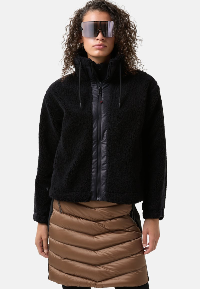 Black fleece jacket with a zipper and high collar, paired with a brown insulated puffy skirt featuring a chevron pattern.