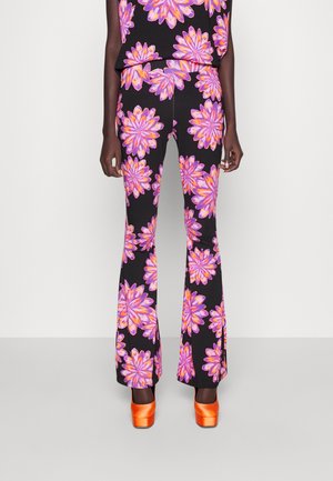 Legging-stijl broek met grote paarse en oranje bloemenprints, gecombineerd met een bijpassend topje en feloranje plateauhakken.