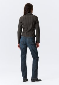 Gestreepte blazer in donker groen en zwart, getailleerd ontwerp met lange mouwen, gecombineerd met blauwe jeans en zwarte enkelboots.