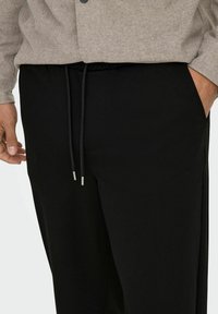 Mustad mustad joggingupüksid, elastse vöökohtaga, millel on hõbedased tipud ja küljetaskud. Pehme, kerge kangatekstuur.