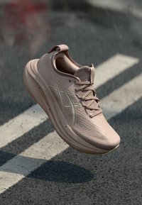 Svijetloružičasta trkaća cipela s teksturiranim gornjim dijelom, zaobljenim vrhom i mrežastim podstavljanjem. Sadrži zlatni logotip i vezivanje putem čipkastih pertli.