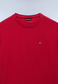 Maglietta rossa in cotone con scollo rotondo e maniche corte. Presenta un piccolo logo ricamato al centro a sinistra sul petto. Texture liscia.