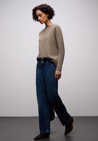 Béžový pletený svetr s dlouhými rukávy v kombinaci s tmavě modrými džíny s širokými nohavicemi. Hnědé kotníkové boty na podpatku doplňují outfit.