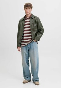 Chaqueta de cuero verde con cuello, polo a rayas burdeos y blanco debajo, y pantalones vaqueros de pierna ancha en azul claro. Zapatos beige tipo slip-on.