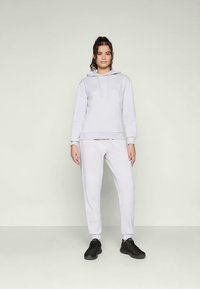 Felpa leggera grigia con coulisse e tasca frontale, abbinata a pantaloni jogger grigi chiari coordinati. Tessuto morbido e vestibilità rilassata, indossata con sneakers nere.