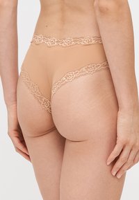 Hnedá spodná bielizeň s čipkovým lemovaním. Elastický, hladký materiál s kvetinovými čipkovými doplnkami pozdĺž pásu. Nízky strih, priliehajúci strih.