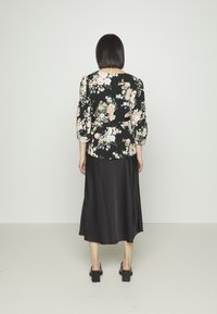 Blusa preta com estampado floral, apresenta mangas bufantes e uma cintura ajustada, combinada com uma saia longa de cetim preta. Textura suave com padrões florais.