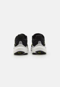 Zapatillas deportivas negras con parte superior texturizada, suela blanca acolchada y detalles en color amarillo brillante, que exhiben un diseño moderno y elegante.