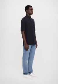Marineblå polo skjorte med teksturert mønster, korte ermer og svart krage, kombinert med lyseblå jeans og hvite joggesko.
