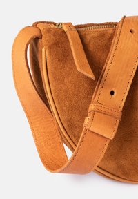 Brown suede crossbody bag featuring a leather strap with visible stitching and a gold zipper. Smooth leather accents enhance the design.
