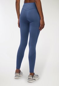 Niebieskie legginsy o wysokim stanem wykonane z elastycznej tkaniny, charakteryzujące się gładką teksturą, zakrzywionymi szwami i dopasowanym krojem, w połączeniu z jasnymi sneakersami.