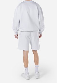 White sweatshirt and shorts set made of soft fabric. Loose fit with cuffed sleeves and shorts. Worn with white sneakers and grey socks.