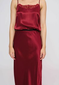 Abito in satin bordeaux con bordatura in pizzo sul collo, spalline regolabili e un design lungo e liscio con una vita in elastico nero.