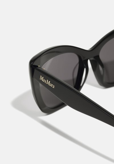 Lunettes de soleil oversized noires avec une finition brillante, dotées de verres foncés et d'une marque "MaxMara" en doré sur la branche. Design angulaire et texture lisse.