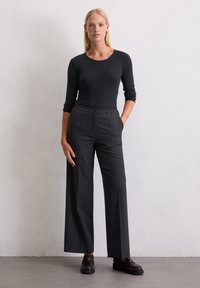 Schwarzes, geripptes Langarmoberteil kombiniert mit hoch taillierten, weiten schwarzen Hosen. Das Outfit umfasst schwarze Schuhe mit glatter Textur und minimalistischem Design.