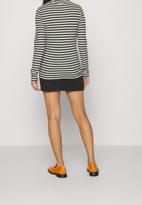 Langärmliges Hemd mit schwarz-weißen Streifen, kombiniert mit einem schwarzen Denim-Minikilt und orangefarbenen Ballerinas. Sichtbare Nähdetails.