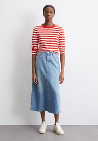 Rot-weißt gestreiftes Langarmoberteil, hoch sitzender hellblauer Jeansrock, weiße Sneaker mit sichtbarem vorderem Nahtdetail.