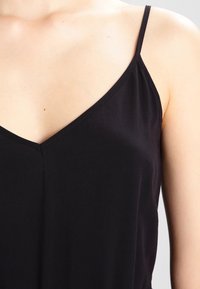 Närbild av en person som bär en svart ärmlös topp med tunna axelband och V-ringning.