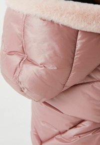 Lyserød pufferjakke med blank finish, der har en blød, lyserød faux fur krave og quiltede sektioner over stoffet.