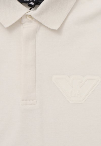 Polo bianco in cotone, con colletto testurizzato e logo in rilievo sul lato sinistro del petto. Tessuto liscio con design classico.
