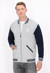 Jachetă bomber gri cu mâneci bleumarin, închidere cu fermoar, buzunare laterale, manșete și tiv ribbată, având un grafic cu ancora și detaliu de scriere.