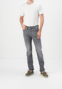 Szare dżinsy z denimu o zwężanym kroju, z pięcioma kieszeniami, lekko wyblakłe, zestawione z białym t-shirtem z okrągłym dekoltem i zielonymi zamszowymi butami.