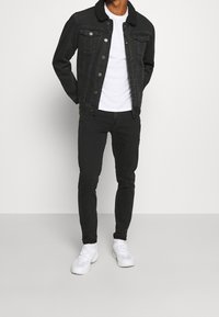 Chaqueta de mezclilla negra con un collar texturizado forrado de pelo, combinada con una camiseta blanca ajustada y jeans skinny negros. Zapatillas blancas completan el atuendo.