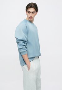 Ανοιχτό μπλε φούτερ με στρογγυλή λαιμόκοψη και ριμπ μανσέτες, συνδυασμένο με γκρι ανοιχτό φούτερ παντελόνι. Λείο ύφασμα, μινιμαλιστικός σχεδιασμός.