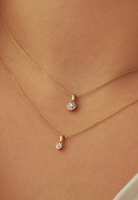 Two delicate gold chains with small round diamond pendants resting on smooth skin at the neck and upper chest.
