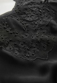 Fekete selyem anyag, amely bonyolult virágos csipkével díszített, gyöngyökkel kiegészítve. A csipke hálós textúrájú és hullámos szélű.