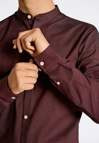 Bordeaux knoopshirt met een mandarincol, voorzien van een textuurstof en witte knopen op de manchetten en het knoopsluiting.