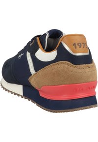 Tmavě modré tenisky s semišovými detaily, béžovým podpatkem a červenou podrážkou. Obsahují síťované panely a detaily s logem, mají zaoblenou špičku a polstrovaný límec.